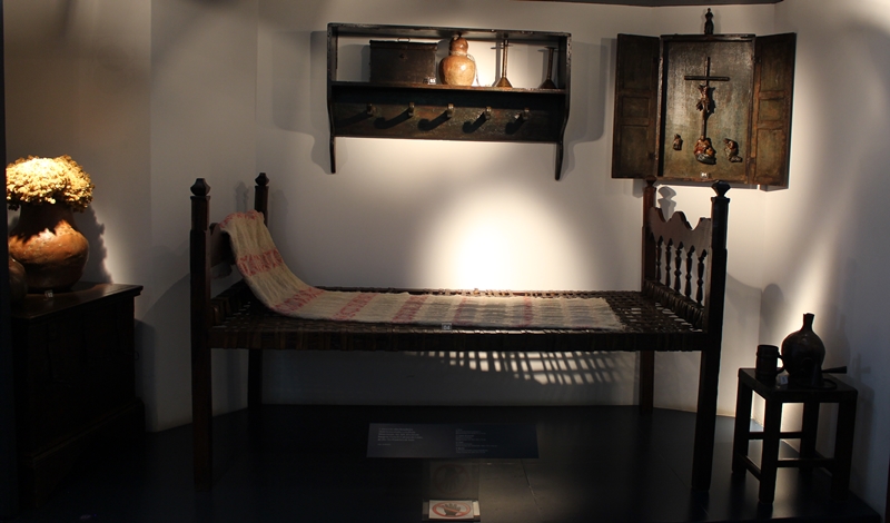 Reconstituição de um quarto simples, com uma cama, uma mesinha, um baú e um oratório singelo - exposto no Museu do Oratório, em Ouro Preto.
